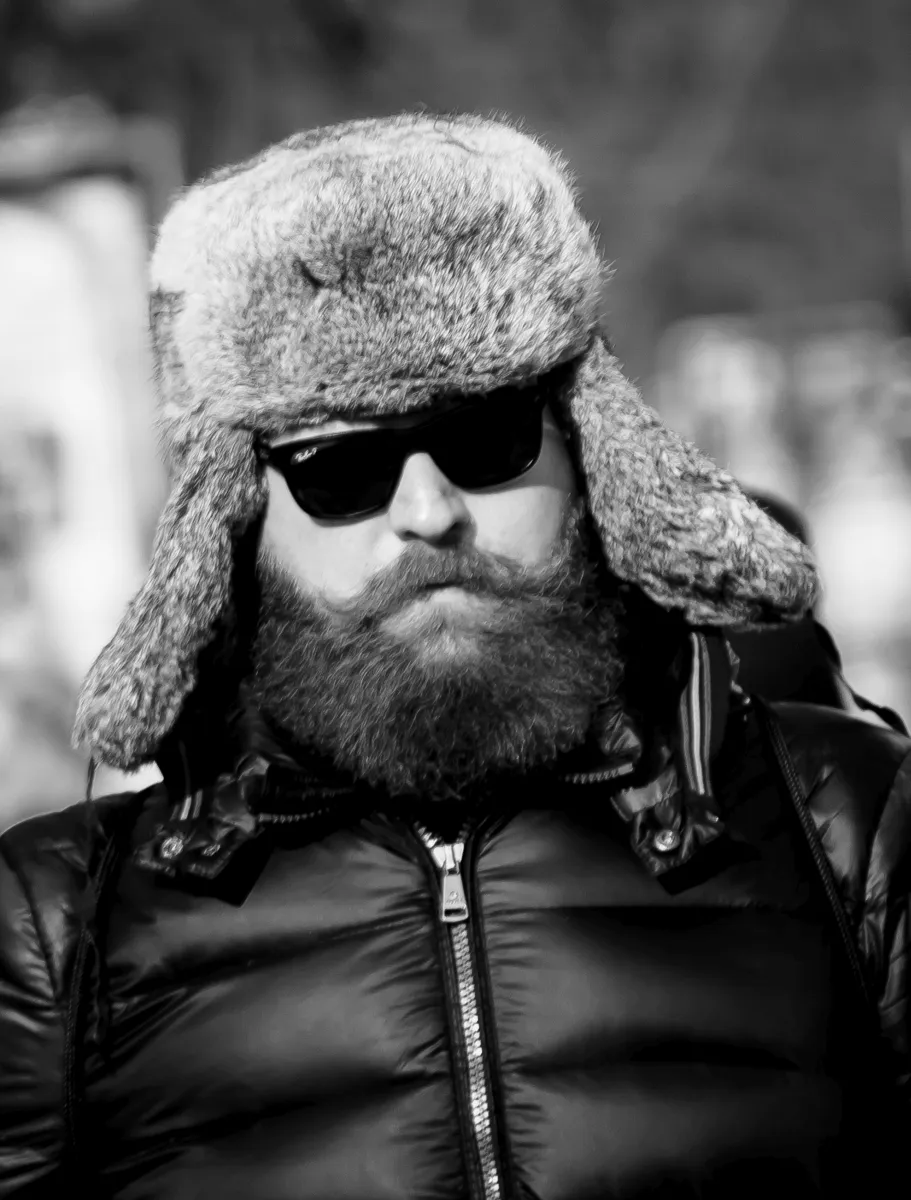 Bearded man in sunglasses and a fur hat facing the camera in winter light